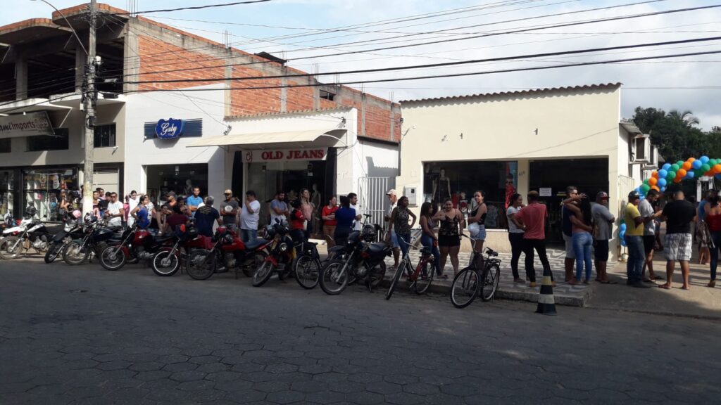 Dezenas de pessoas aguardando a matrícula em frente às lojas, com motos enfileiradas no meio-fio
