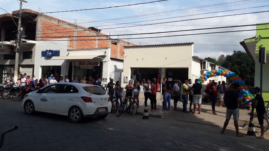 Carro passando em frente à fila de pessoas que aguardam a abertura das matrículas