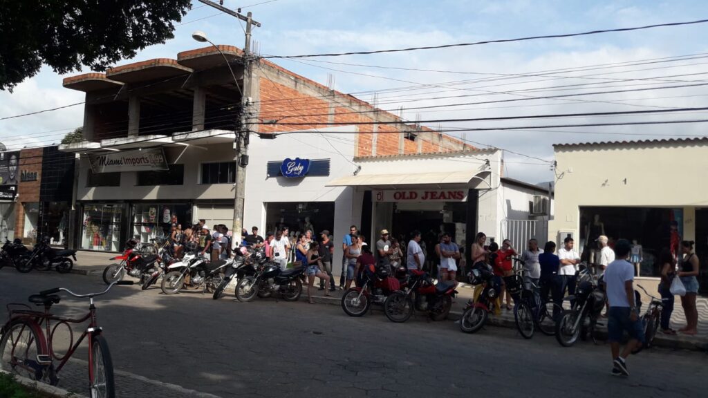 Vista ampla da rua com a fila de candidatos e motos estacionadas ao longo da calçada