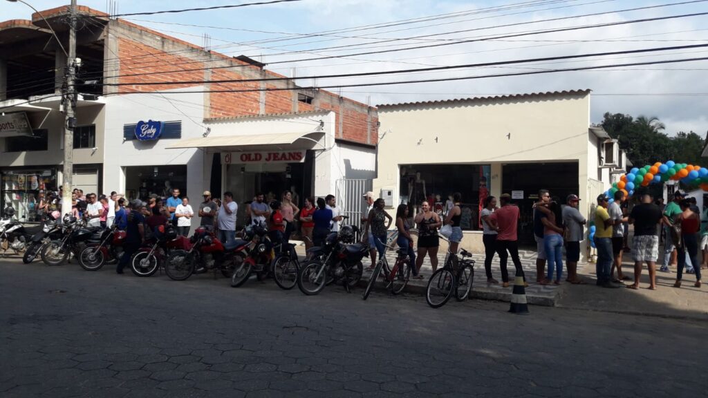 Fila de candidatos com motos e bicicletas diante da autoescola decorada com balões